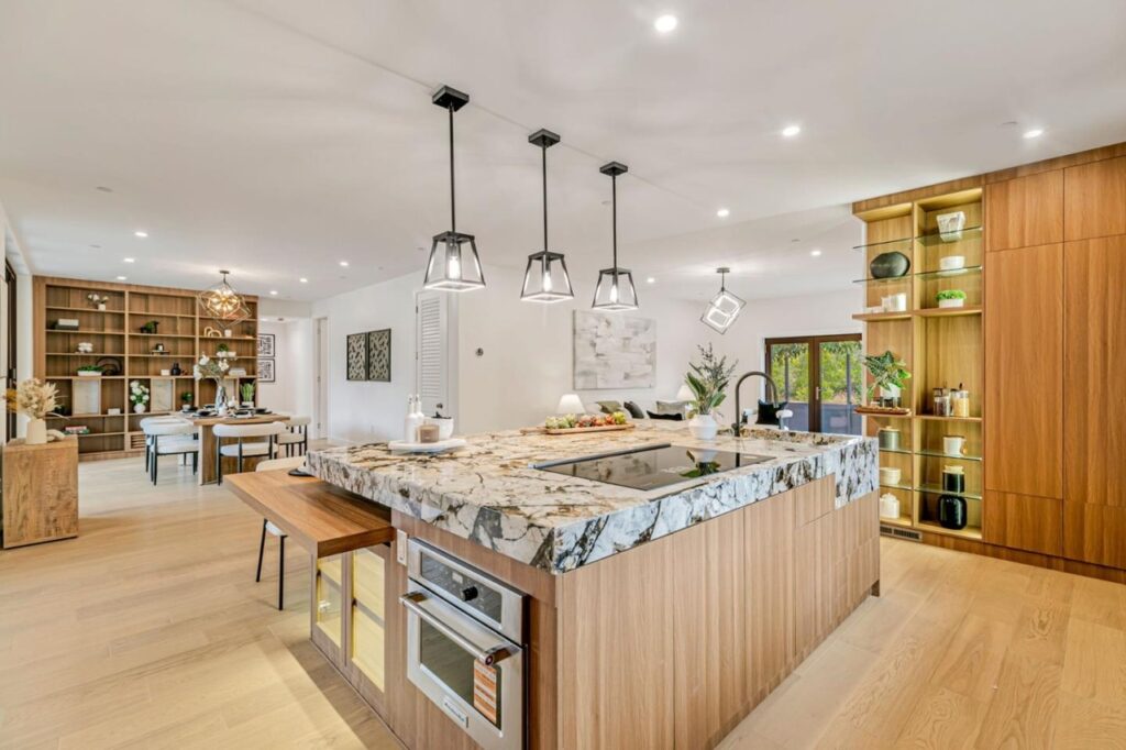 Modern open-concept kitchen and dining area inside the luxurious Hawthorne home in Campbell, California, featuring a striking granite-topped kitchen island, built-in wooden cabinetry, and a well-lit dining space in the background.